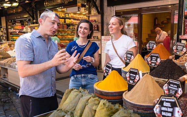 Tour guide explaining spices to tourists at a market on the Taste of Two Continents Food Tour.