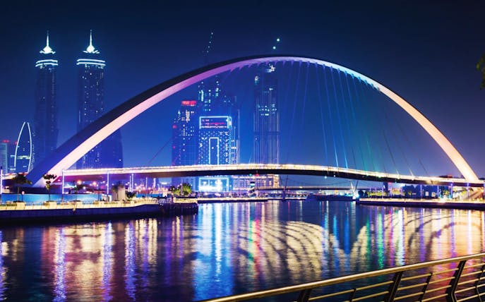 Dubai Water Canal bridge illuminated at night with city skyline.