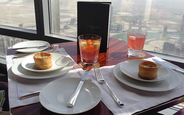 Dining setup with pastries and drinks overlooking Dubai skyline at night.
