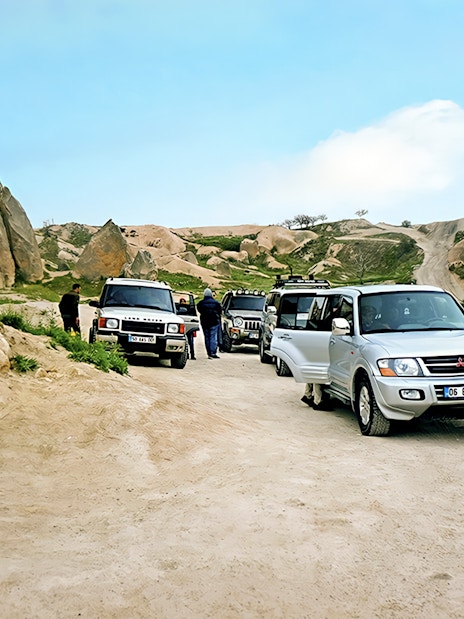Off-road jeeps parked on a dirt path in Cappadocia with rocky landscape in the background.
