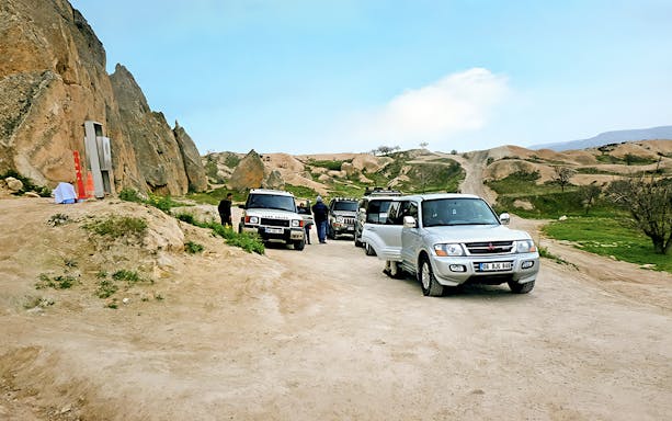 Off-road jeeps parked on a dirt path in Cappadocia with rocky landscape in the background.