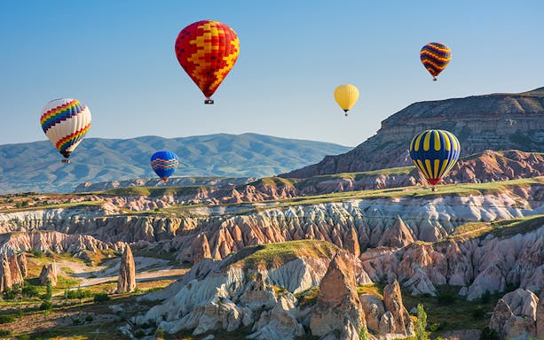 Hot air balloons over Cappadocia's unique rock formations during a hop-on hop-off bus tour.