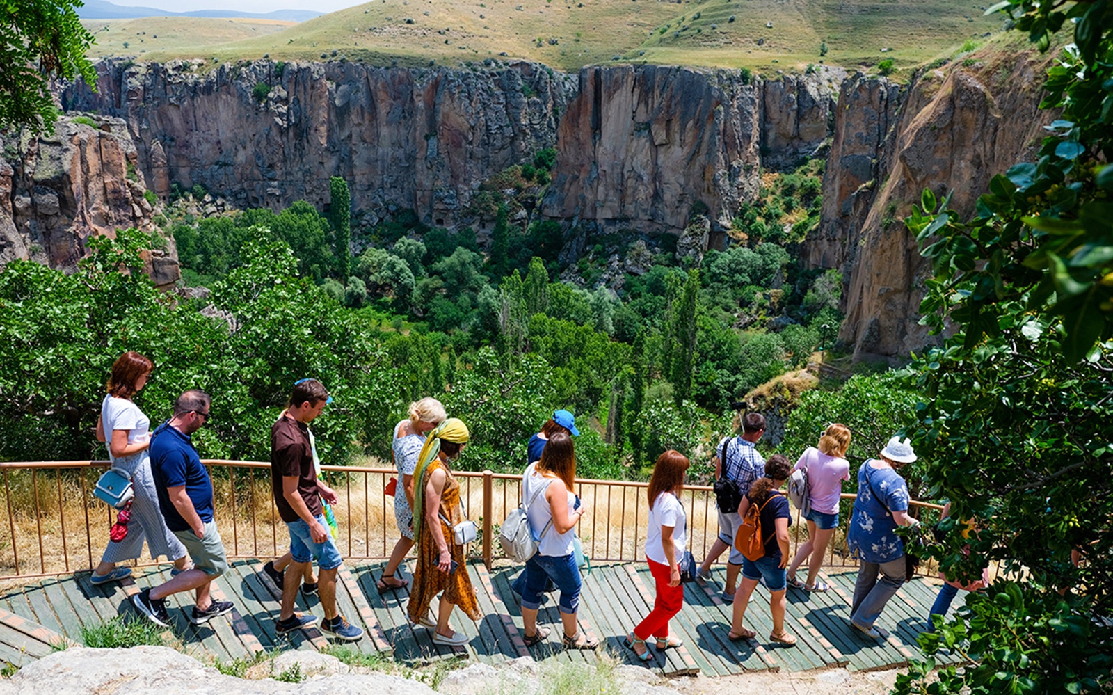 Tourists walking along a path in Ihlara Valley, Cappadocia, surrounded by lush greenery and cliffs.