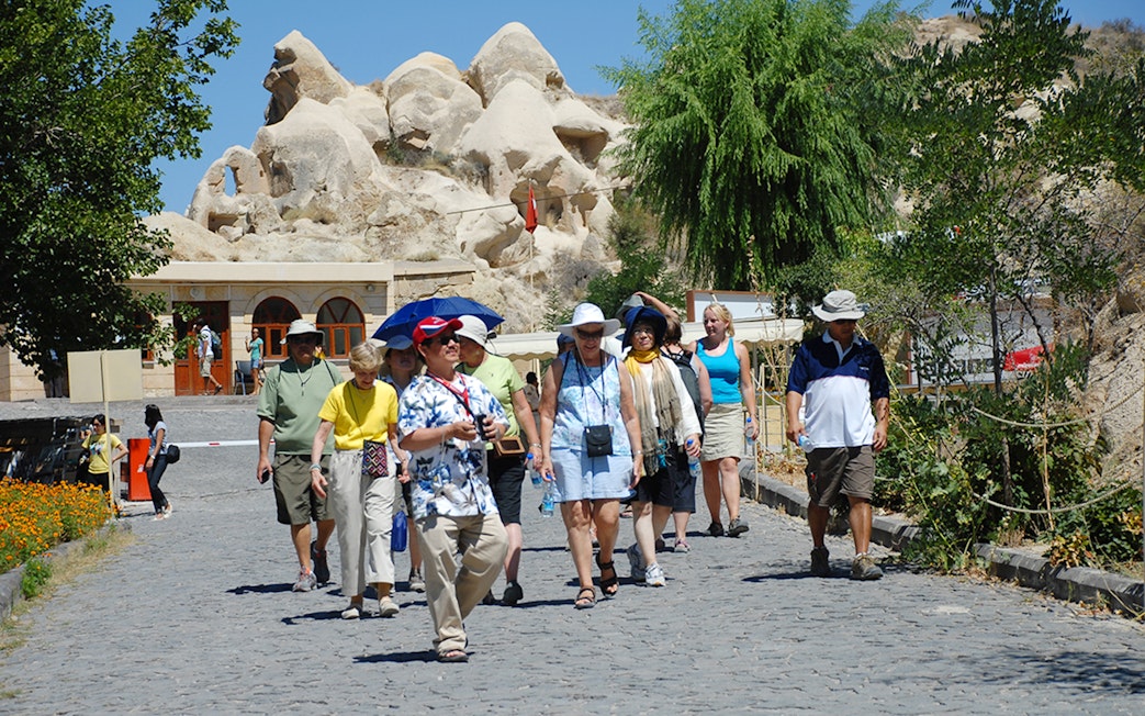 Tourists walking at Göreme Open-Air Museum, Cappadocia, with rock formations in the background.