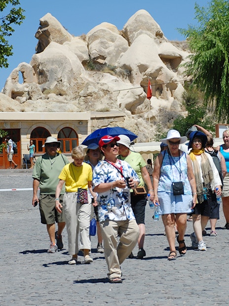 Tourists walking at Göreme Open-Air Museum, Cappadocia, with rock formations in the background.