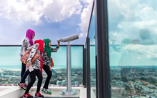 Visitors using a telescope at The Shore Sky Tower with city view below.