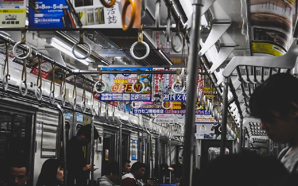 Tokyo subway interior with passengers and overhead advertisements.