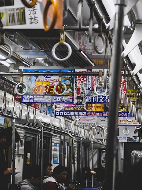 Tokyo subway interior with passengers and overhead advertisements.