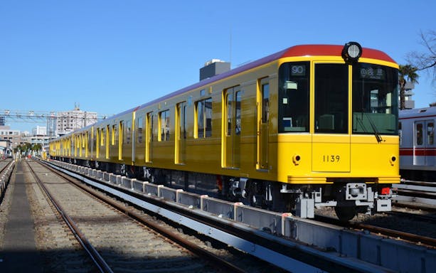 Yellow Tokyo subway train on tracks under a clear sky.