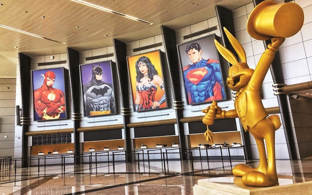 Warner Bros. World™ Abu Dhabi entrance with superhero posters and golden cartoon statue.