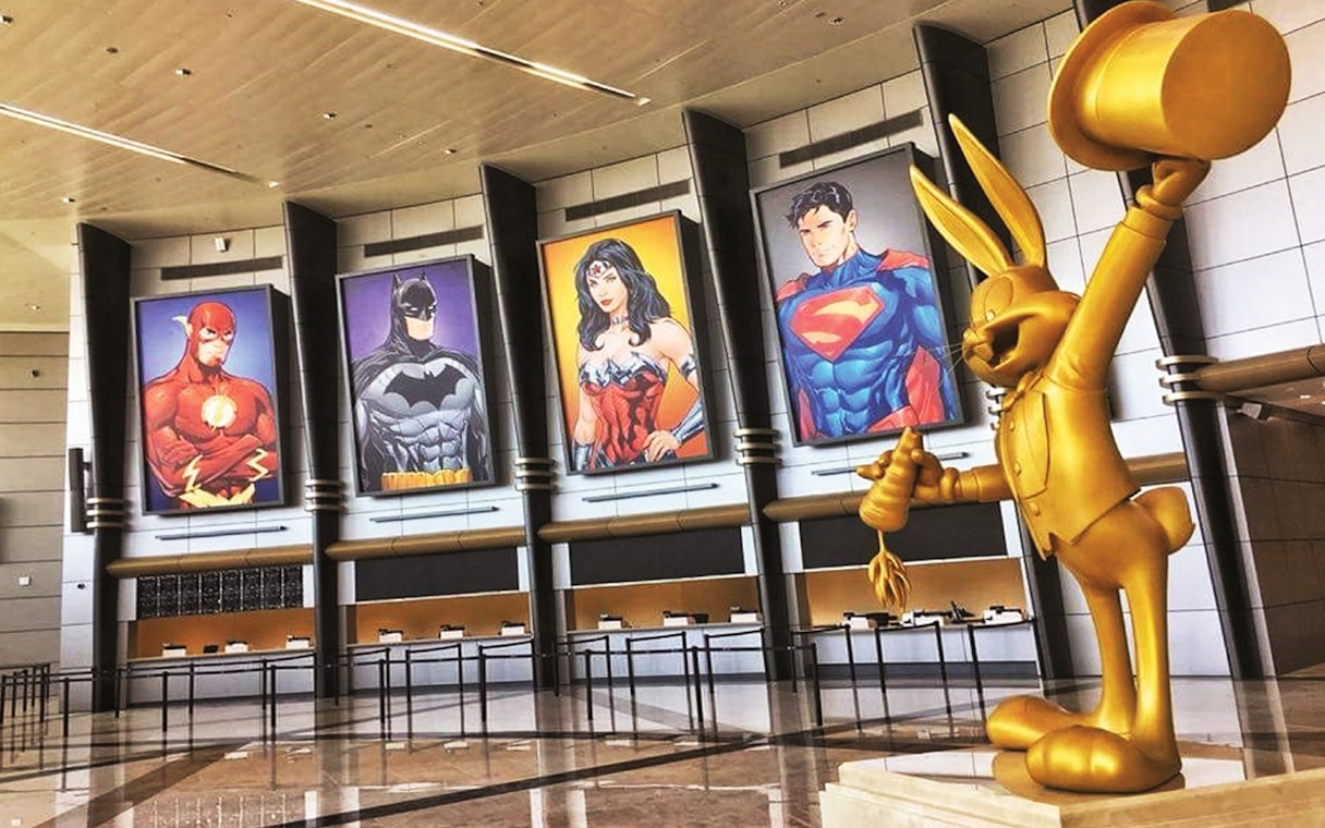 Warner Bros. World™ Abu Dhabi entrance with superhero posters and golden cartoon statue.