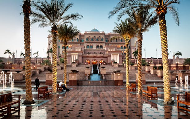 Exterior view of Emirates Palace in Abu Dhabi with palm trees and fountains.