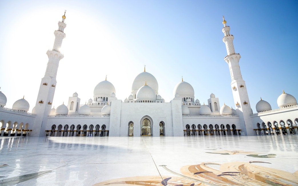 Sheikh Zayed Mosque in Abu Dhabi with white domes and minarets under a clear blue sky.