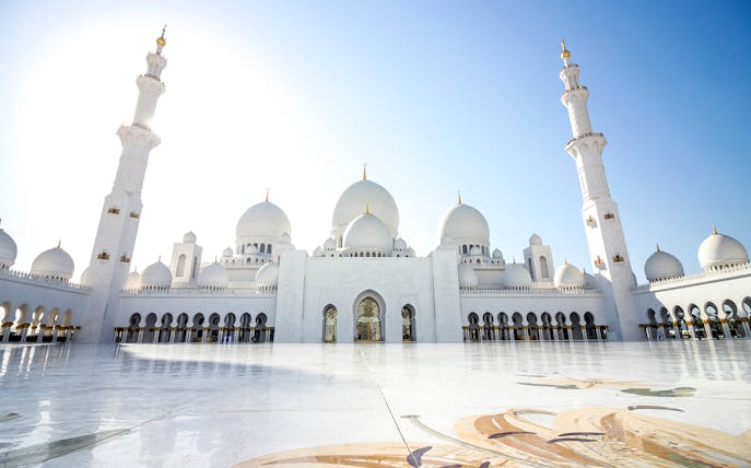 Sheikh Zayed Mosque in Abu Dhabi with white domes and minarets under a clear blue sky.
