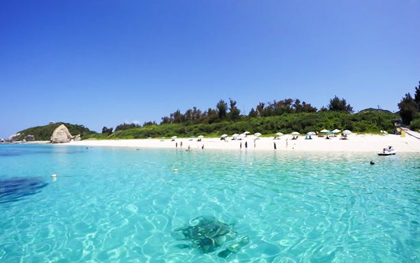 Aharen Beach with clear turquoise water and people enjoying sea-bathing in Okinawa, Japan.