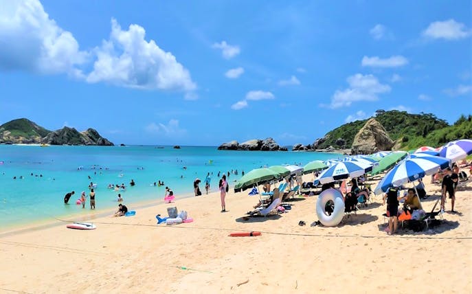Visitors enjoying Aharen Beach with umbrellas and clear blue water, Tokashiki Island, Japan.