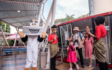 Visitors at Menara Taming Sari, Melaka, greeted by a mascot and staff in traditional attire.