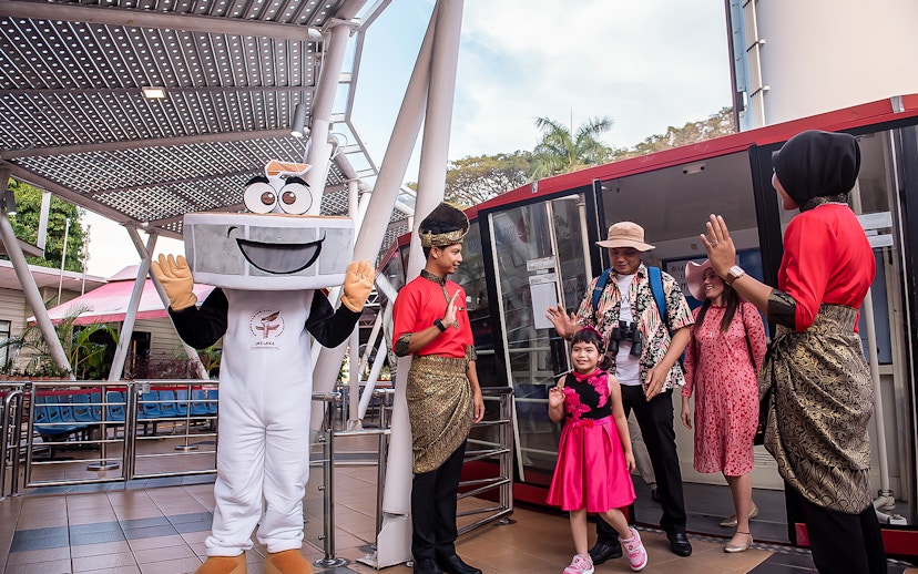 Visitors at Menara Taming Sari, Melaka, greeted by a mascot and staff in traditional attire.