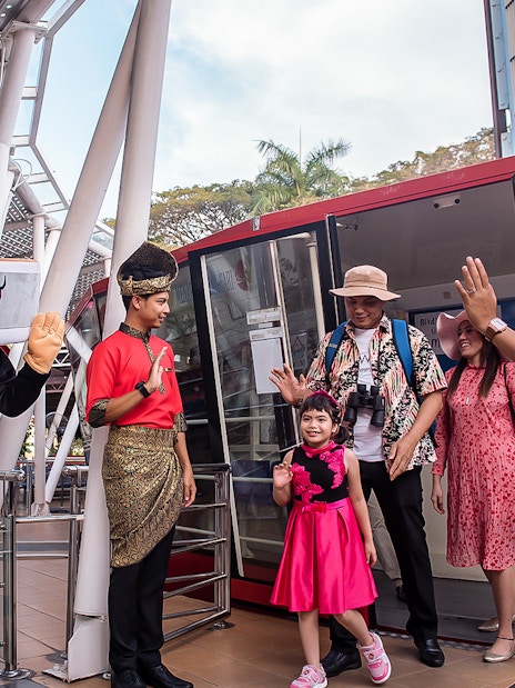 Visitors at Menara Taming Sari, Melaka, greeted by a mascot and staff in traditional attire.