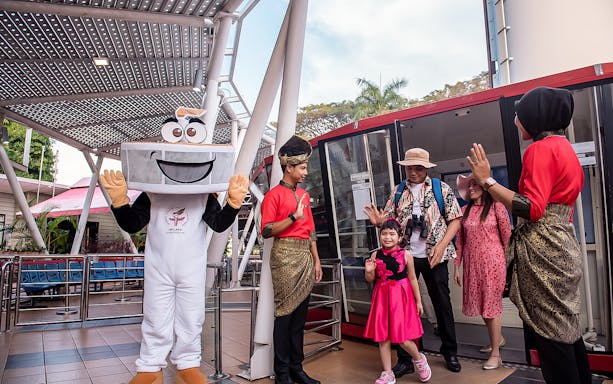 Visitors at Menara Taming Sari, Melaka, greeted by a mascot and staff in traditional attire.