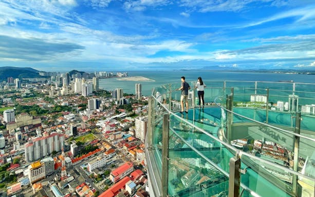 Visitors on the glass skywalk at The Top Penang with city and ocean views.