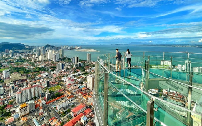 Visitors on the glass skywalk at The Top Penang with city and ocean views.