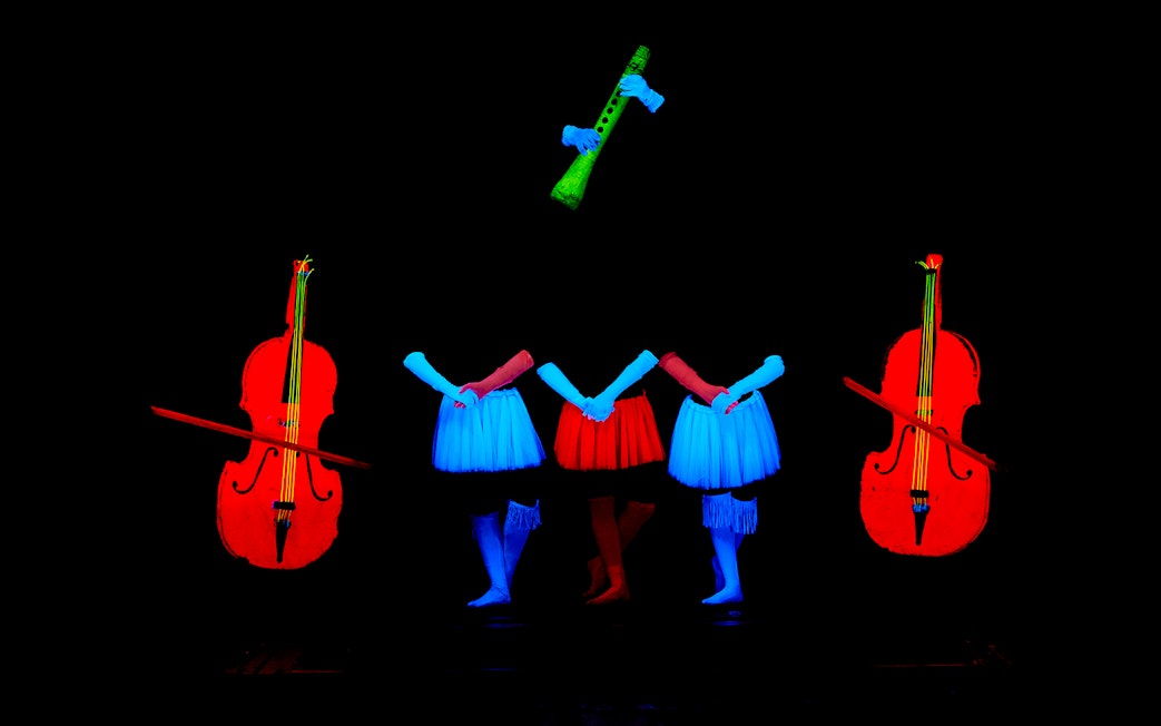 Performers in neon costumes with glowing instruments at WOW Show Black Light Theater.