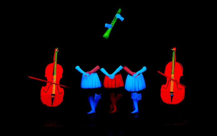 Performers in neon costumes with glowing instruments at WOW Show Black Light Theater.