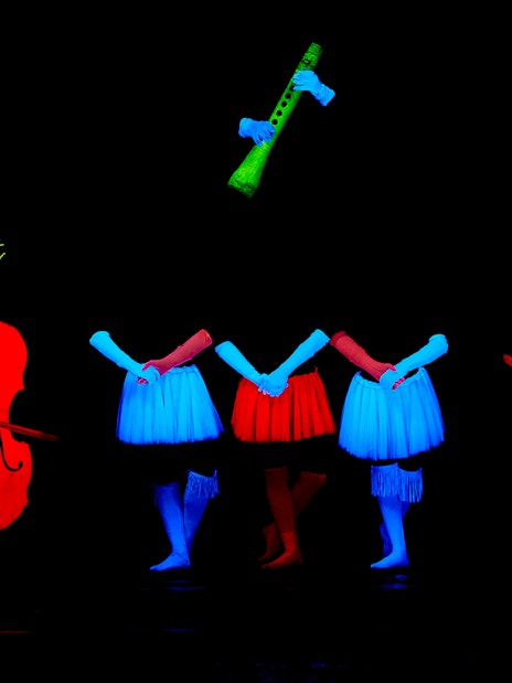 Performers in neon costumes with glowing instruments at WOW Show Black Light Theater.