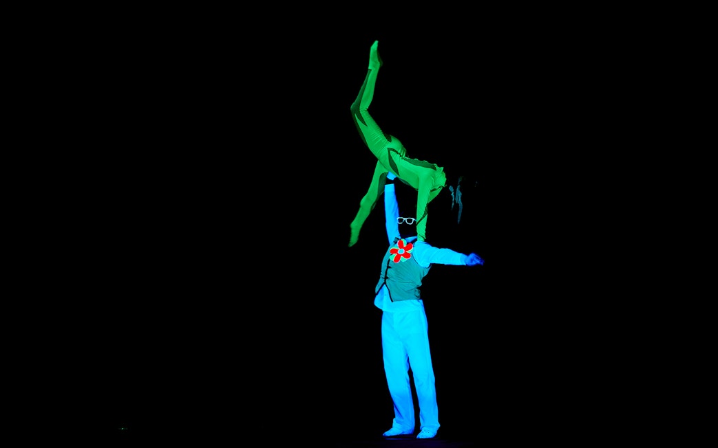 Performer lifting another in neon costumes at WOW Show Black Light Theater.