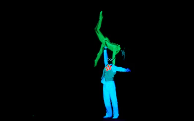 Performer lifting another in neon costumes at WOW Show Black Light Theater.