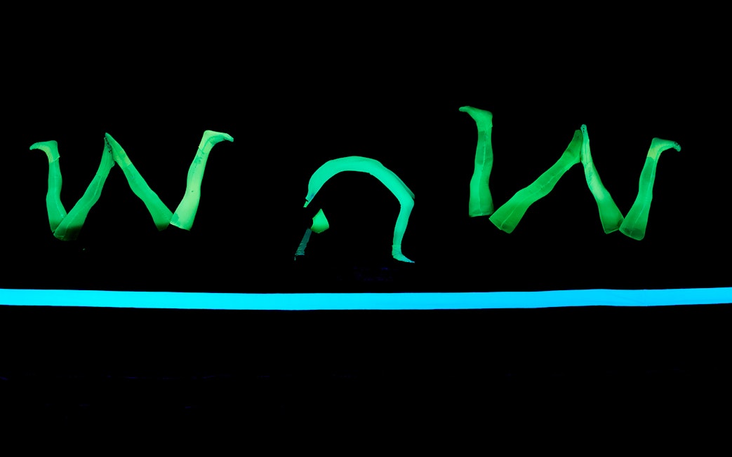 Glowing green figures performing at WOW Show Black Light Theater.