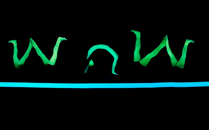 Glowing green figures performing at WOW Show Black Light Theater.