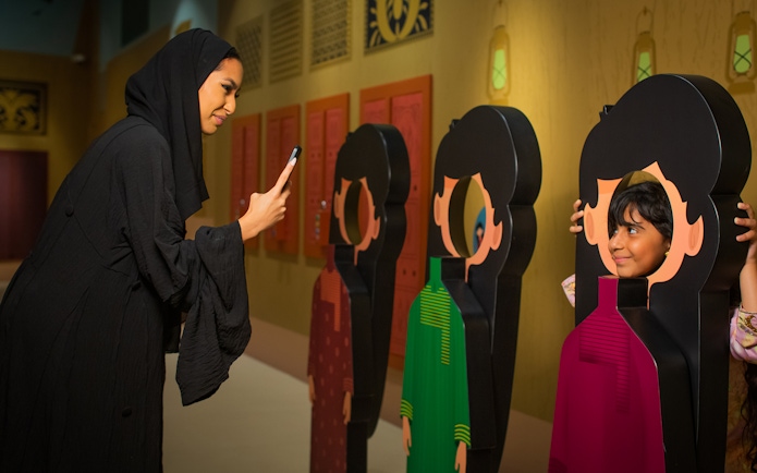 Visitor photographing child posing with cutout at Al Shindagha Museum.
