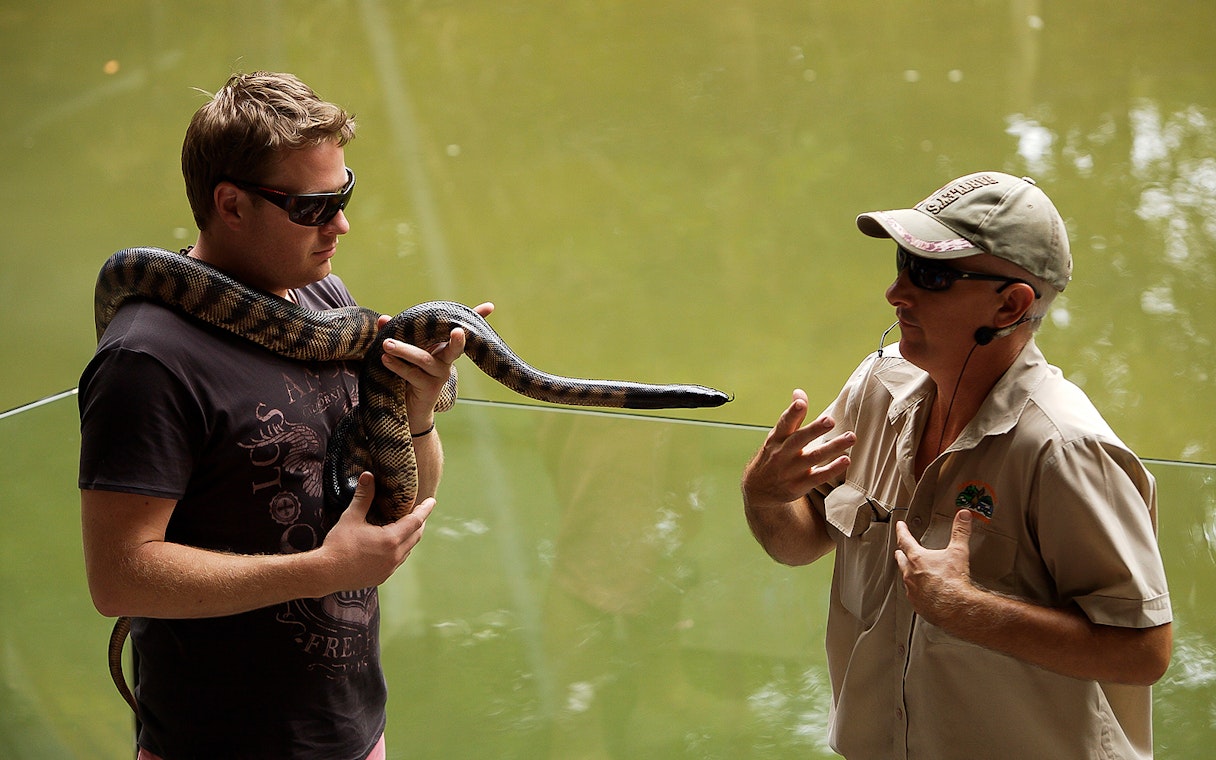 Man holding a snake with a guide at Hartley’s Crocodile Adventures.