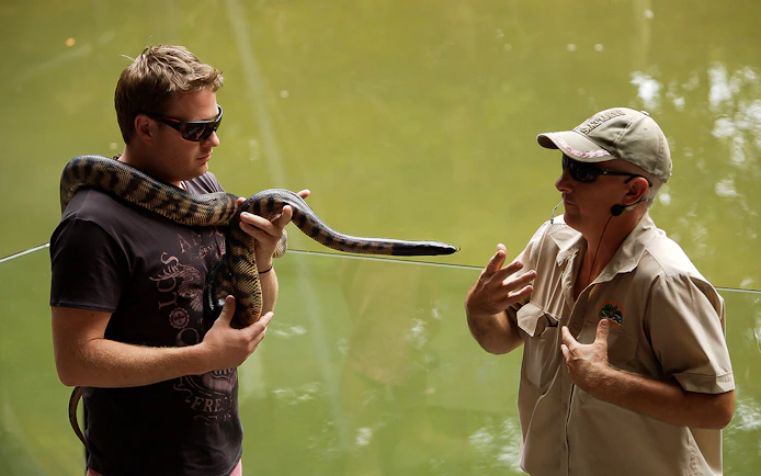 Man holding a snake with a guide at Hartley’s Crocodile Adventures.