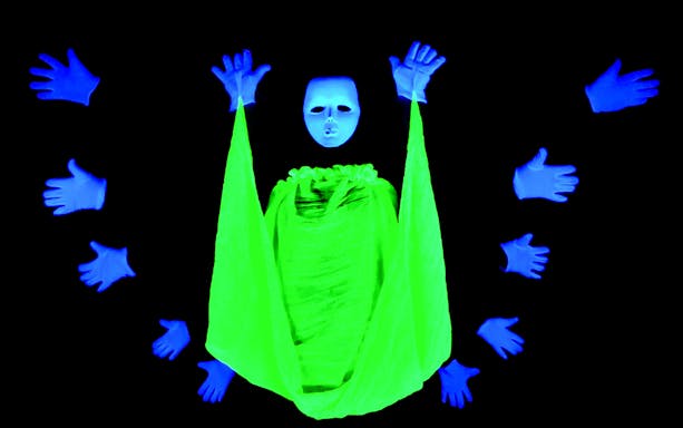 Performer in neon costume with floating hands at Magic Phantom Black Light Theatre.
