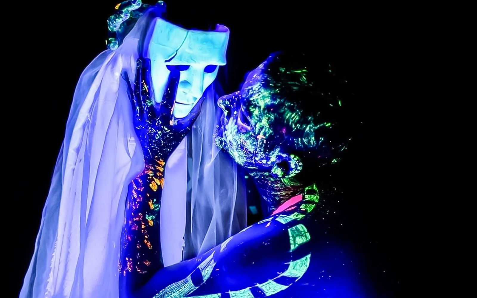 Performer in neon body paint holding a glowing mask at Magic Phantom Black Light Theatre.