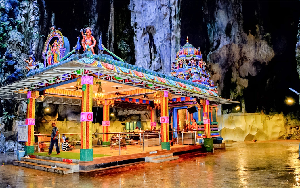 Colorful temple inside Batu Caves, Malaysia, with intricate carvings and visitors exploring.