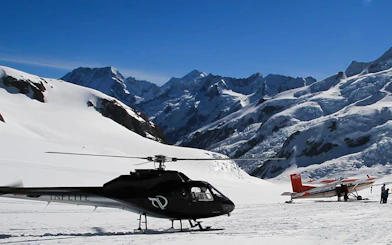 Helicopter and small plane on snowy Mt Cook with Southern Alps backdrop.