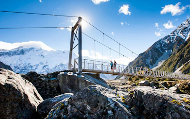 Hikers crossing a suspension bridge with Mt Cook in the background, New Zealand.
