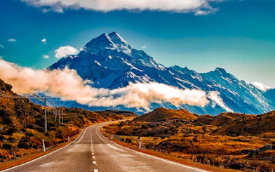 Road leading to Mt Cook with snow-capped peaks and clouds, New Zealand.