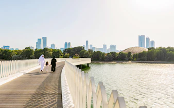 Family walking on Al Noor Island bridge with Sharjah skyline in the background.