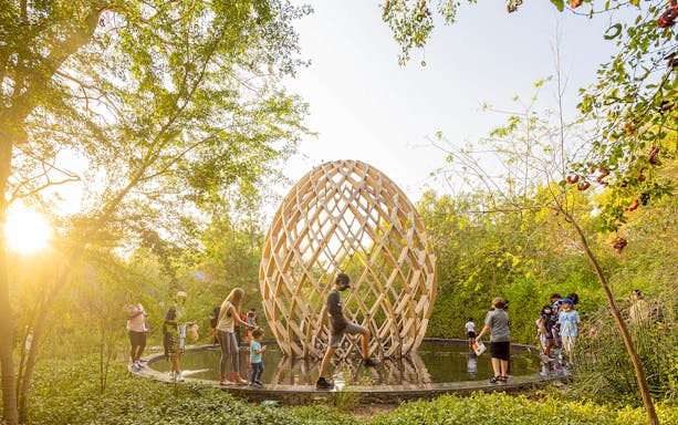 Visitors exploring Al Noor Island's wooden sculpture surrounded by lush greenery.