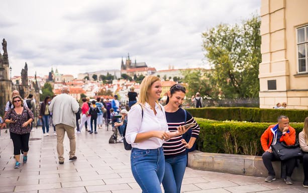 Tourists exploring Charles Bridge with Prague Castle in the background.