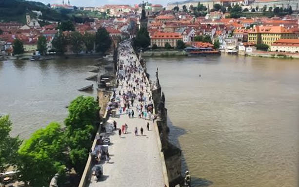Crowds walking on Charles Bridge in Prague with cityscape views.