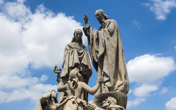 Statues on Charles Bridge in Prague under a blue sky.