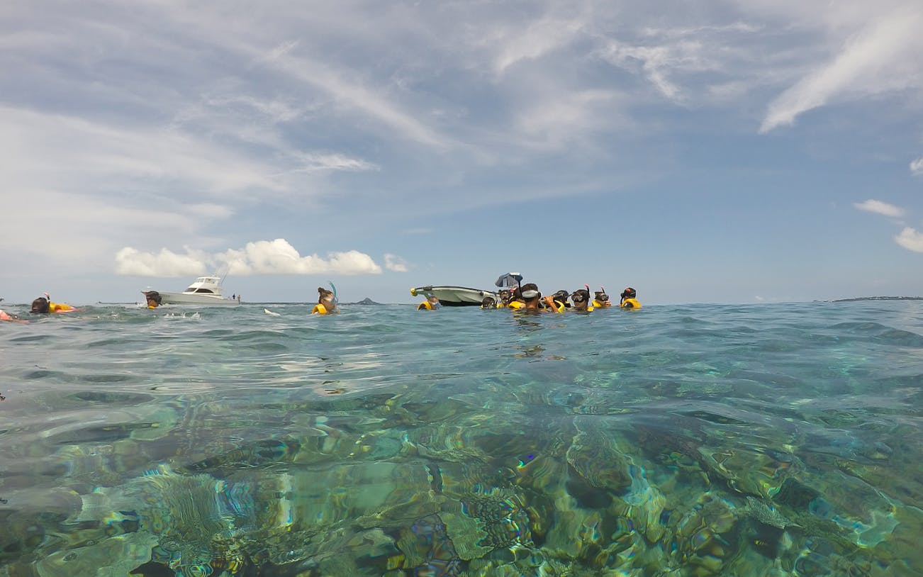 Snorkelers in clear water near a boat on Minna Island day trip.