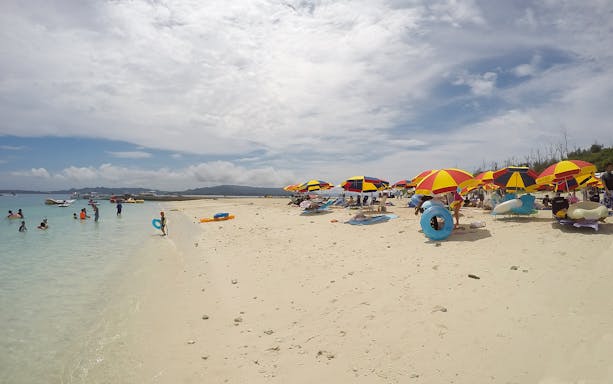 Beachgoers enjoy Minna Island with colorful umbrellas and clear water.