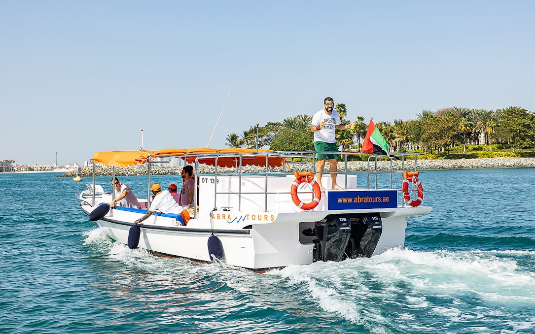 Private small group on a boat cruise in Dubai with UAE flag and coastal view.